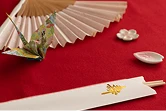 赤い布の上に置かれた扇子や折り鶴、祝い箸