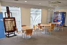 丸テーブルと椅子、自動販売機が置かれた明るいフリースペース。