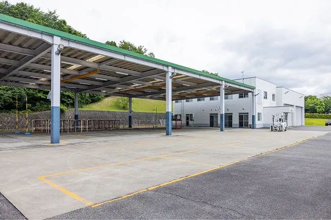 大きな屋根が設置された全天候型の練習エリアと、黄色の区画線が引かれた地面、奥に停められた白色のフォークリフト。