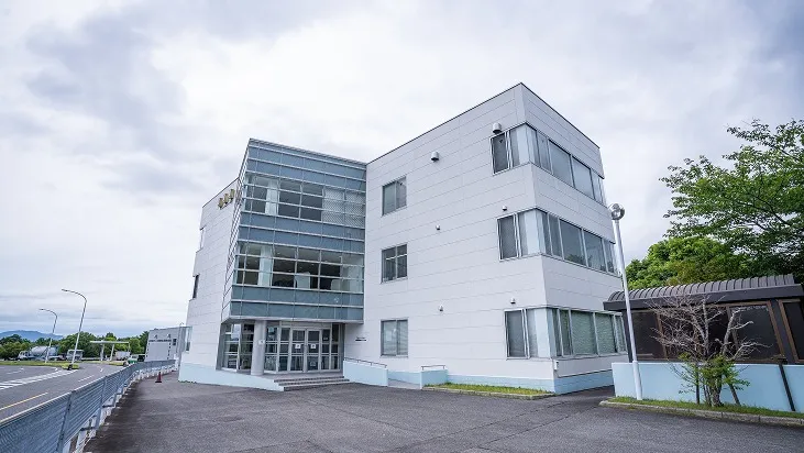 ガラス張りの出入口やスロープを備えた、白い清潔感のある3階建ての研修棟外観。