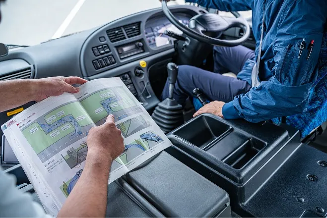 大型車両の運転席で図解テキストを指さしながら指導を受ける様子。