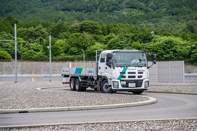 山に囲まれた広い場内コースで、カーブを走行する大型トラック。