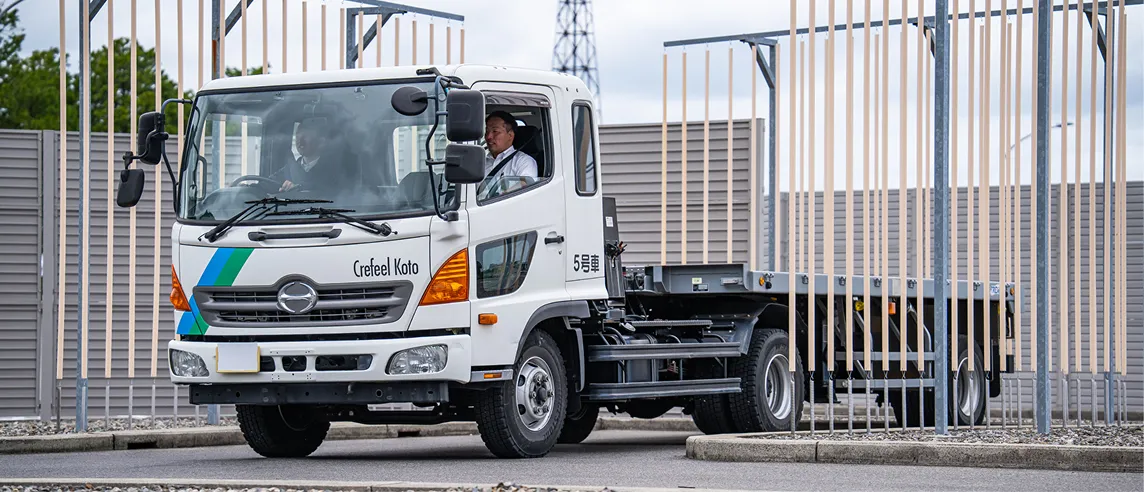 自動車教習所のコース内で、白い牽引トラクタ（ヘッド）を運転する教習生と指導員。