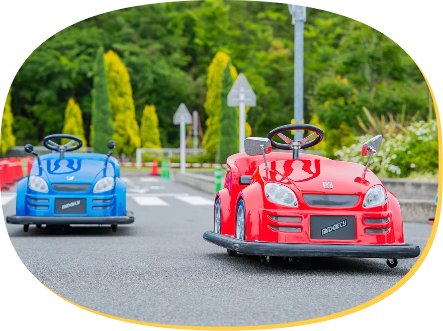 横断歩道や道路標識があるコースを走る、子供用の赤いEVカーと青いEVカー。