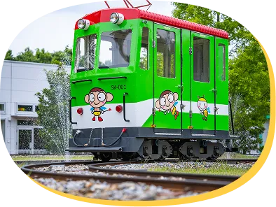 緑豊かな屋外の線路上に置かれた、イラスト付きの小さな電車