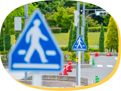 手前に大きく写る横断歩道の標識と、緑豊かな交通コースの風景。