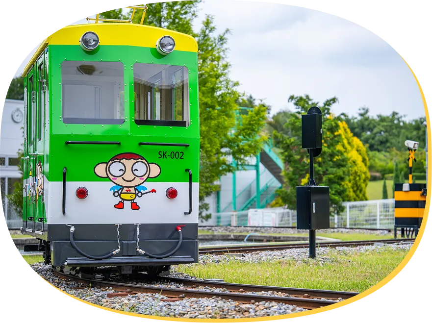 踏切のある線路上を走る、緑と黄色の小型電車「キッズトレイン」。