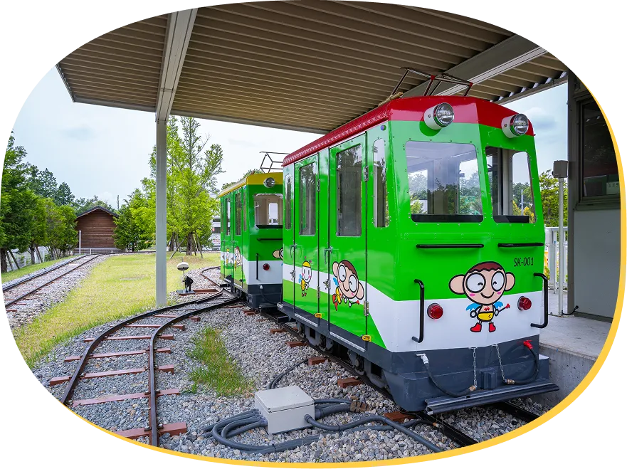 ホームの屋根の下に停車している、緑と赤のキッズトレイン車両。