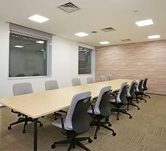 中央に長テーブルとグレーの椅子が対面で並ぶ、グループワークや会議に適した討議室。