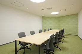 長テーブルとグレーの椅子が対面に並ぶ、グリーンを基調とした明るい雰囲気の討議室。