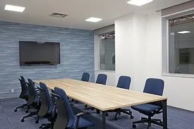 長テーブルと青い椅子が対面に並び、壁面に大型モニターを備えた討議室。
