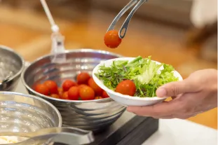 ボウルからトングで生野菜サラダをお皿に盛り付ける様子