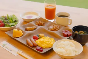 プレートにスクランブルエッグやご飯、味噌汁、ジュースなどが並べられた朝食