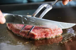 熱々の鉄板の上で肉フォークとナイフをあて、ミディアムレアに焼き上げるステーキ肉