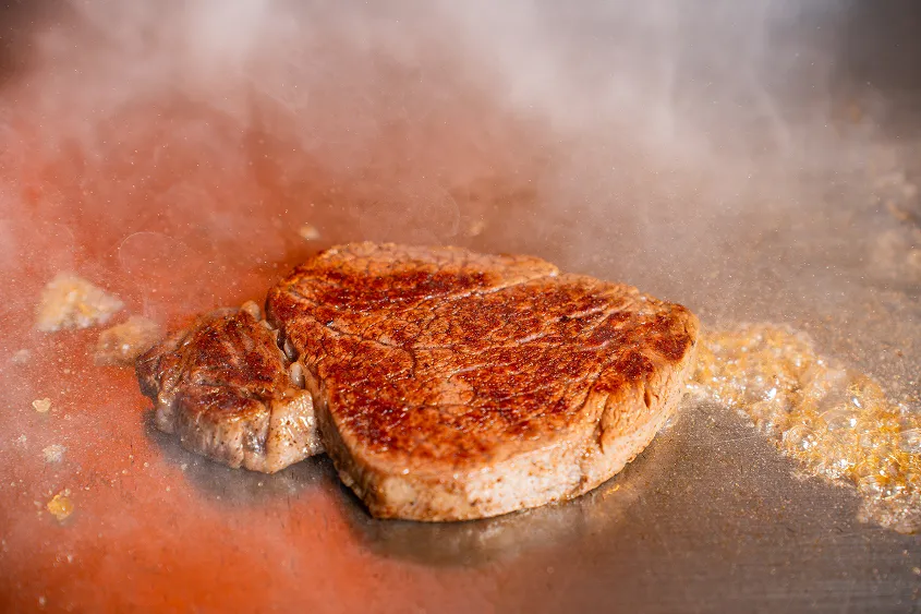 鉄板の上で湯気を立てながら香ばしく焼き上げられる厚切りステーキ肉