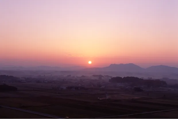 朝もやに包まれた山並みと大地を照らす朝日の美しい風景